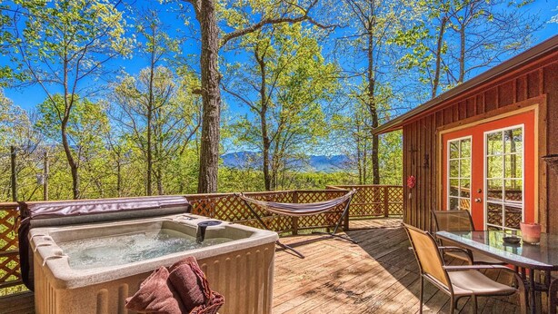 Een houten terras met een jacuzzi, een hangmat en een tafel met stoelen.