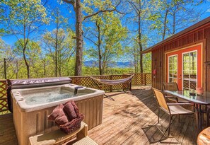 A wooden deck with a hot tub, a hammock, and a table with chairs.