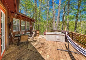 A wooden deck with a hot tub, outdoor seating, and a view of a forest.