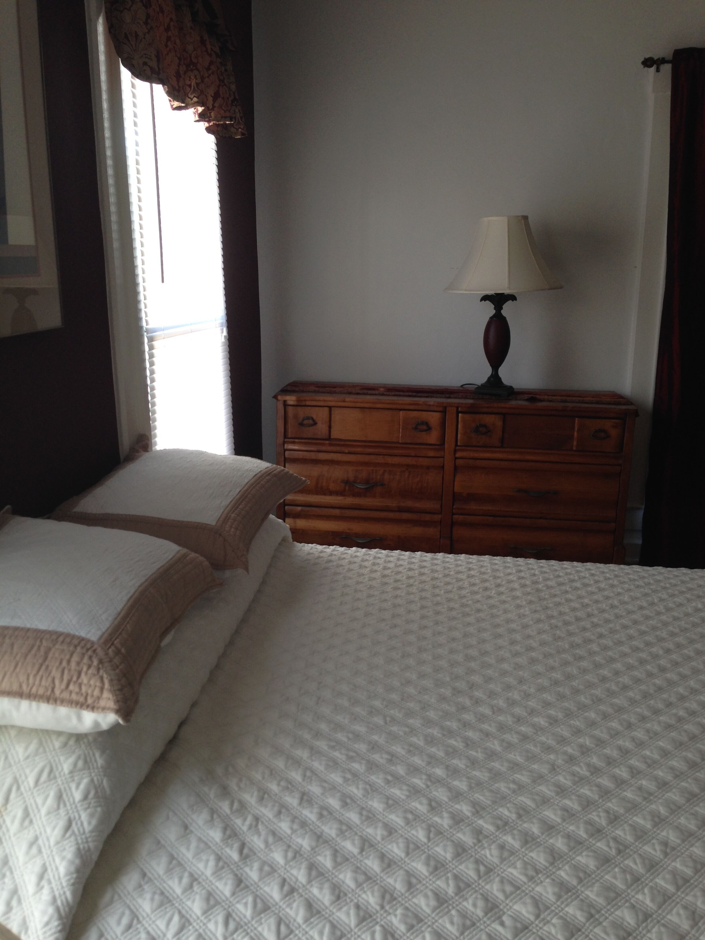 A bedroom with a bed, a wooden dresser, and a lamp.