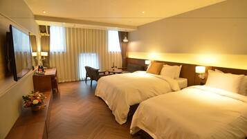 Hotelkamer met twee bedden, een bureau, een stoel, een televisie en een raam met gordijnen.