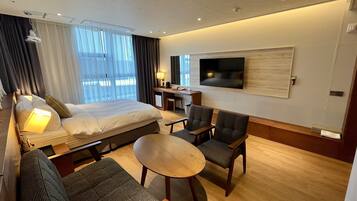 A hotel room with a bed, a desk, a TV, a sofa, and a small table.
