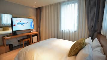 A hotel room with a bed, a TV on a desk, a window with curtains, and a small table with a chair.