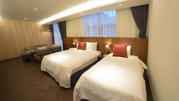 Quarto de hotel com duas camas, um sofá e uma mesinha.