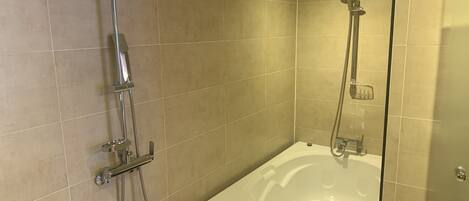 A modern bathroom with beige tiles, a glass-enclosed bathtub, and a shower with a handheld showerhead.