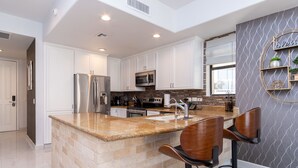 Una cocina moderna con armarios blancos, encimeras de granito, electrodomésticos de acero inoxidable y una isla central con taburetes de bar.