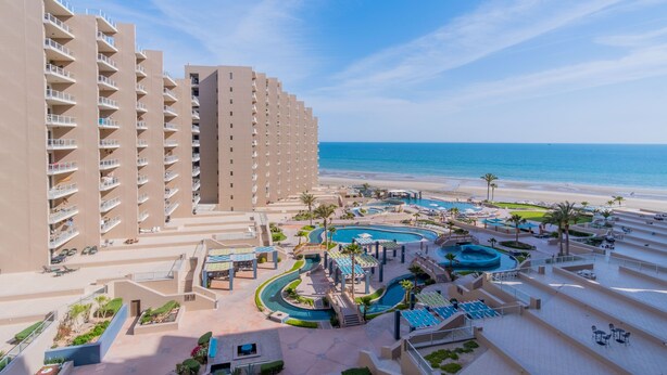 Un complejo turístico con varias piscinas, una playa y edificios de gran altura.