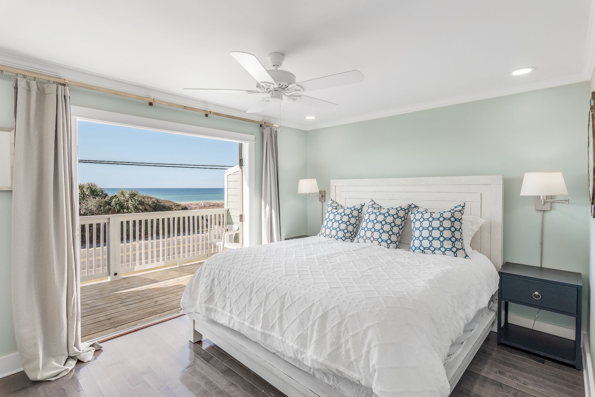 A bedroom with a large bed, a ceiling fan, and a view of the ocean.
