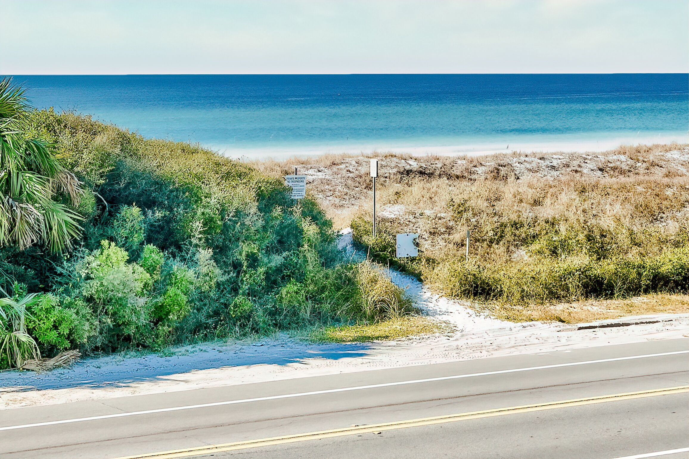 Carretera costera con vista a la playa, vegetación y un letrero que indica propiedad privada.