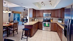A modern kitchen with dark wood cabinets, a granite countertop, stainless steel appliances, and a dining area with wooden chairs and a chandelier.