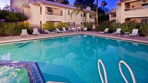 A swimming pool with lounge chairs and a hot tub, surrounded by a building with balconies and a garden.