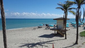 A beach with a lifeguard station, palm trees, and umbrellas. - Want peace and relaxation in a beach area? Then look no further (Hollywood)