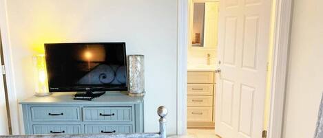 Una habitación con televisor sobre un tocador azul, una pequeña mesa redonda y una puerta que da al baño.
