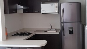 Eine moderne Küche mit dunklen Schränken, einer eingebauten Mikrowelle, einem Edelstahlkühlschrank und einem Gasherd.