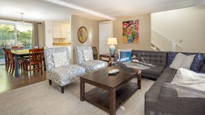 A spacious living room with a dark wooden coffee table, patterned armchairs, a grey sectional sofa, and a dining area with wooden chairs and a table. - Open for the Holidays! Fireplace, Near XC skiing and Wineries, Good for Groups! (Leland)