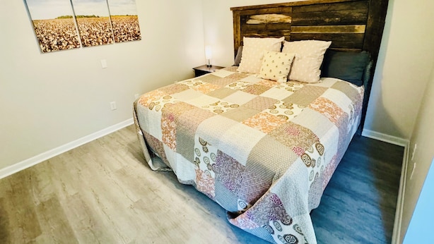 A bedroom with a wooden headboard, a quilted bedspread, and a nightstand.