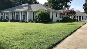 A residential house with a well-maintained lawn, a driveway, and a front yard with a small tree and shrubbery.