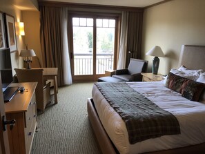 Hotellihuone, jossa on sänky, työpöytä, tuoli, kannettava tietokone, lamppu ja suuri ikkuna, josta on näkymä ulos.