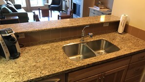 Una cocina con encimeras de granito, pileta de acero inoxidable y muebles de madera.