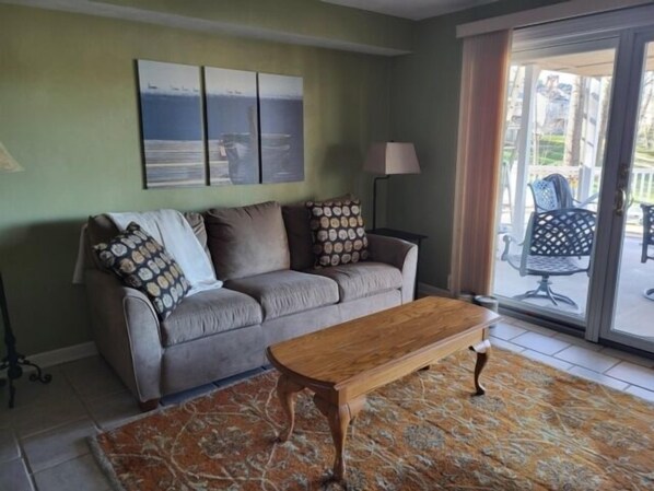 A living room with a sofa, a wooden coffee table, a patterned rug, and a view of the outdoors through a glass door. - Wifi, hot tub, pool table, air hockey, and fully loaded boat house!. This is Lake Lxury! (Moneta)