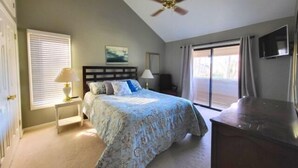 A bedroom with a bed, a ceiling fan, a window with blinds, a painting, a desk with a lamp, and a TV on the wall. - Wifi, hot tub, pool table, air hockey, and fully loaded boat house!. This is Lake Lxury! (Moneta)