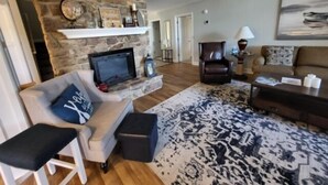 A living room with a stone fireplace, a television, a sofa, a patterned rug, and a staircase. - Wifi, hot tub, pool table, air hockey, and fully loaded boat house!. This is Lake Lxury! (Moneta)