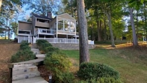 A two-story house with a balcony, surrounded by trees and a wooden pathway leading to the entrance. - Wifi, hot tub, pool table, air hockey, and fully loaded boat house!. This is Lake Lxury! (Moneta)