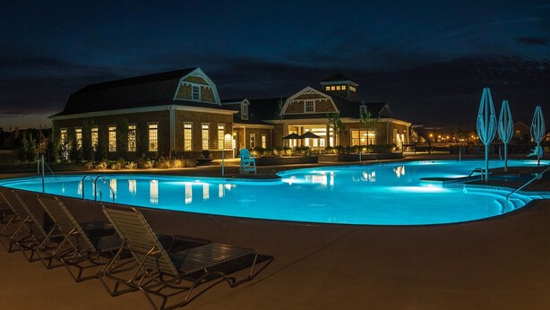 Ein Schwimmbad mit Liegestühlen, ein Gebäude mit großen Fenstern und eine gut beleuchtete Außenansicht bei Nacht.
