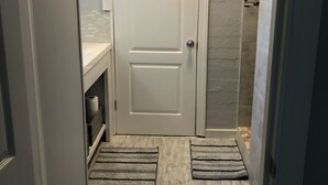 Un baño con una puerta blanca, un perchero, una zona de ducha y dos felpudos en el suelo.