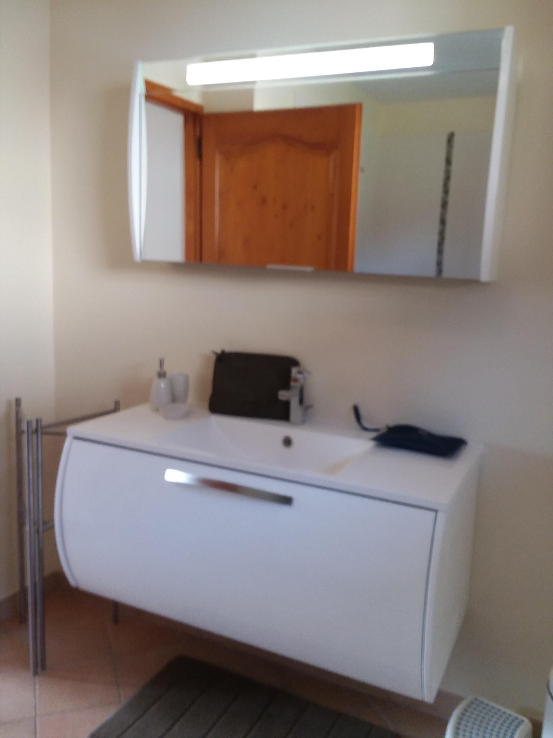 Un baño con un lavabo blanco, un espejo encima y una puerta de madera.