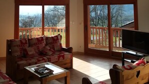Un salon spacieux avec de hauts plafonds, de grandes fenêtres, une terrasse en bois et un coin salon confortable.