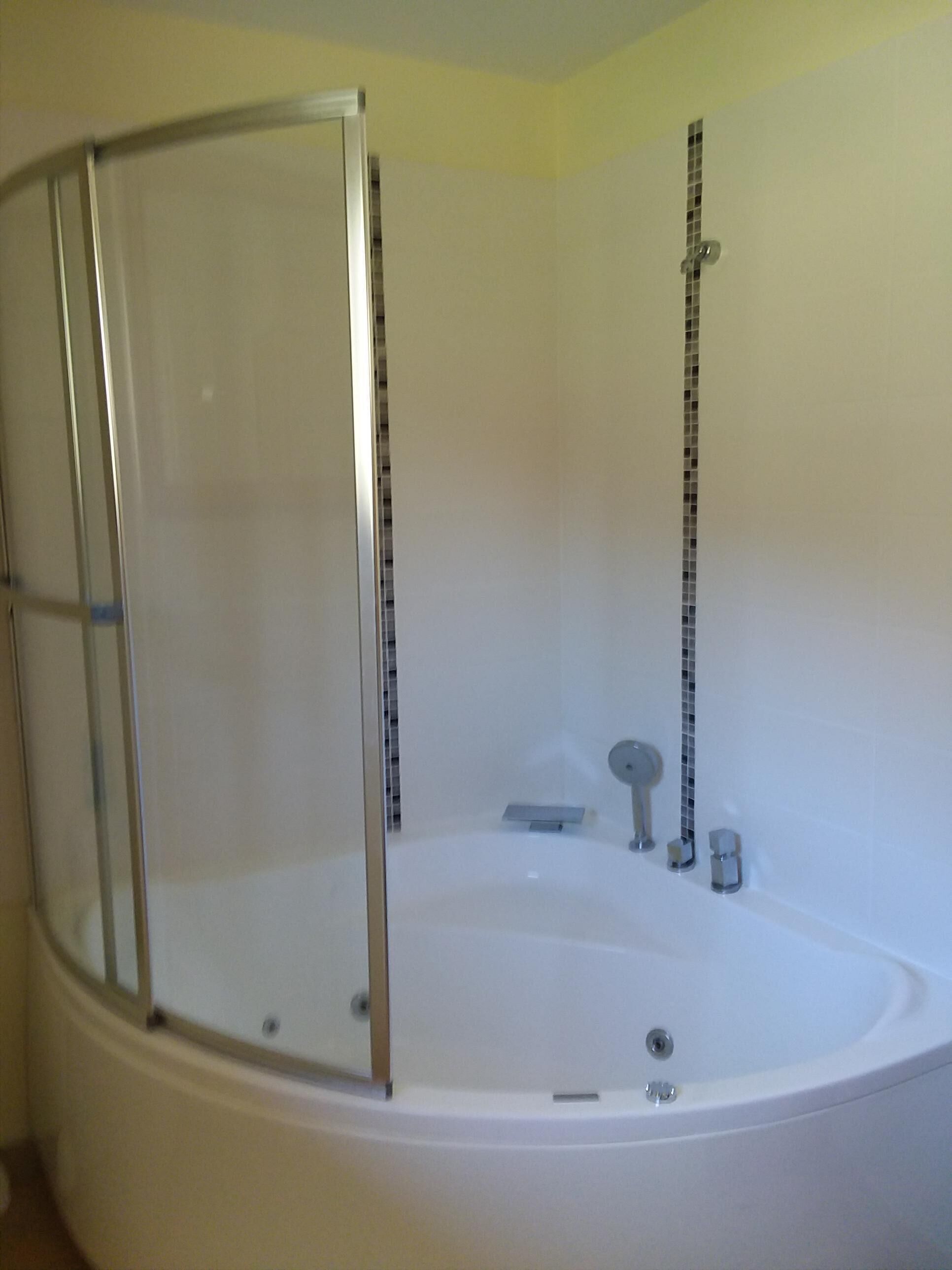 A large, empty bathtub with a glass enclosure, a showerhead, and a control panel.