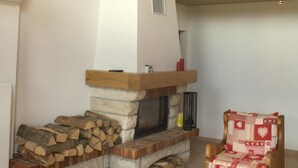 Un salon chaleureux avec une cheminée en pierre, des poutres apparentes et un fauteuil en bois.
