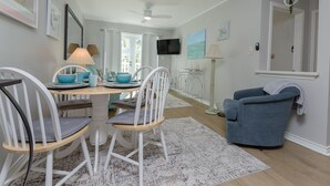 A dining area with a white table and chairs, a blue armchair, and a television on the wall.