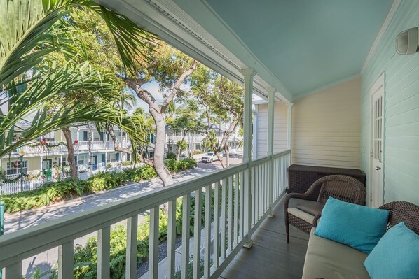 A porch with a view of a street and trees, a wicker chair, and a sofa with cushions. - SOUTHARD COMFORT at The Truman Annex in Key West (Key West)