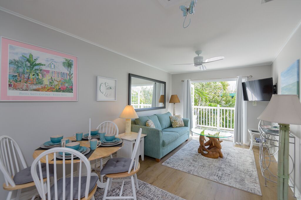 Ein gemütliches Wohnzimmer mit einem blaustürkisenen Sofa, einem Esstisch mit Stühlen, einem Fernseher und einem Balkon mit Aussicht.