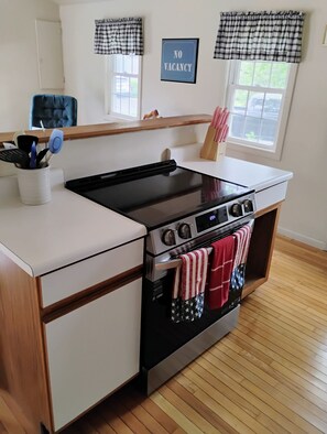 Una cocina con estufa de acero inoxidable, armarios de madera y una ventana con el letrero 'NO VACANCY'.