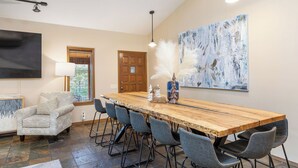 A spacious room with a long wooden table, six chairs, a patterned armchair, a television, and a large abstract painting on the wall. - Private Pool - Pickleball - Hot Tub - Theatre Room (Branson)
