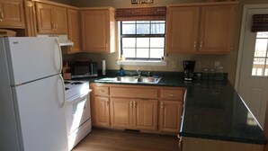 A kitchen with wooden cabinets, a white refrigerator, a stove, a microwave, a sink, and a window with blinds.