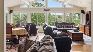 A spacious living room with a high ceiling, large windows, and a ceiling fan. - Stunning Cedar 4 BR , 3 full bath hm with amazing views of the lake & mountains.  Private deep water dock with adjacent floating dock.  Located in the largest NO Wake Cove on the lake, perfect for swimming and kayaking/paddle boarding. (Huddleston)