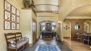 A spacious hall with a wooden bench, a blue patterned rug, and framed botanical prints on the wall.