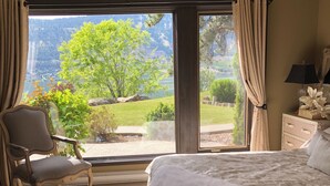 Un dormitorio con una cama grande, una silla y vistas a un lago y montañas a través de una puerta corrediza.