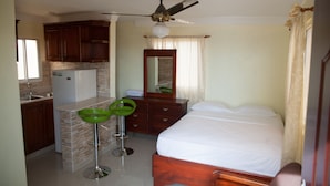 Habitación de hotel compacta con kitchenette, cama, baño y ventilador de techo.