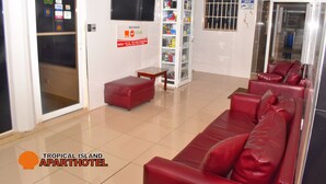 Zona de recepción con un sofá de cuero rojo, una mesita, un minibar y un tablón de anuncios con opciones de pago.