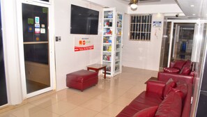 A reception area with a red leather sofa, a small table, a minibar, and a notice board with payment options.