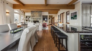 A modern kitchen with a stone fireplace, wooden beams, and a bar area with stools. - Elkhorn Summer Amenities and Mtn Views (Sun Valley)