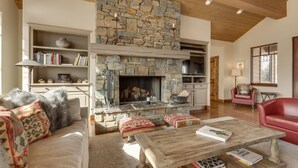 A cozy living room with a stone fireplace, a wooden ceiling, and a comfortable seating area with a red leather chair and a sofa. - Elkhorn Summer Amenities and Mtn Views (Sun Valley)