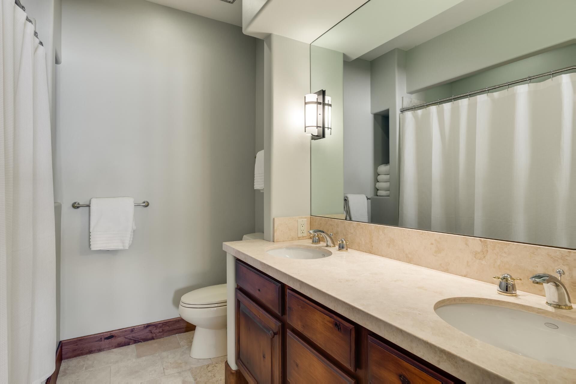 A bathroom with two sinks, a toilet, a shower curtain, and a mirror.