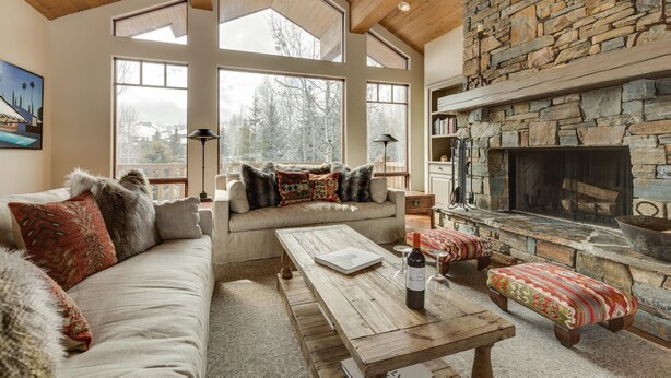 A cozy living room with a stone fireplace, large windows, and a wooden ceiling. - Elkhorn Summer Amenities and Mtn Views (Sun Valley)