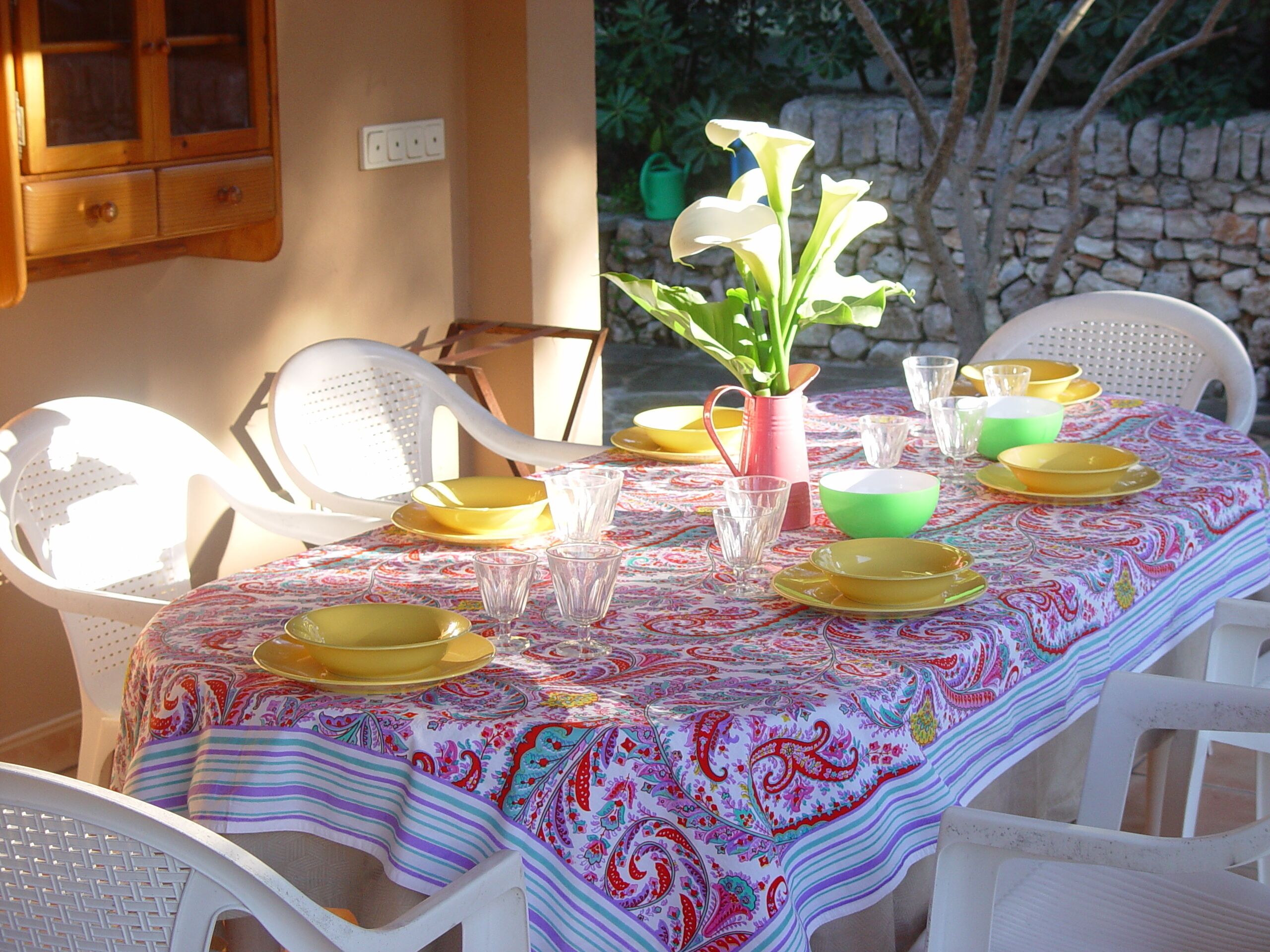 Una mesa de comedor dispuesta con platos amarillos, vasos transparentes y un mantel colorido.